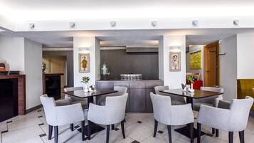 A modern dining area with a central bar, grey upholstered chairs, and a tiled floor.