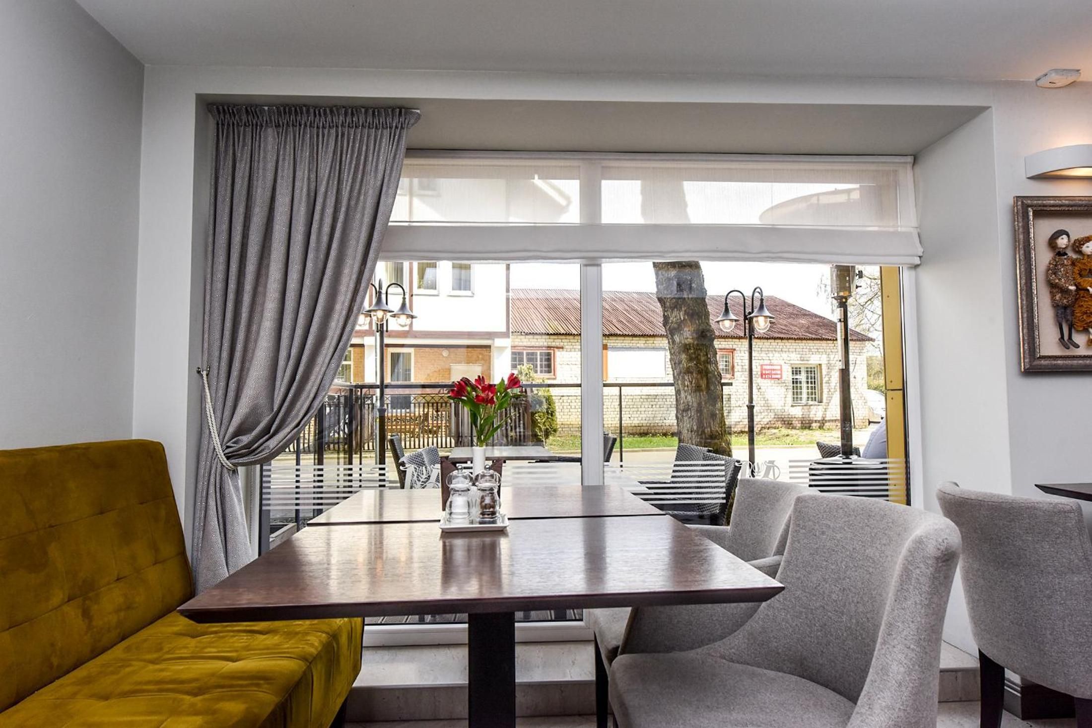 Una sala moderna con un sofá, una mesa de comedor y sillas. Hay un ventanal con cortinas, y una vista al exterior.