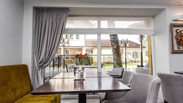 Una sala moderna con un sofá, una mesa de comedor y sillas. Hay un ventanal con cortinas, y una vista al exterior.