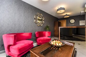 A modern living room with two red upholstered chairs, a wooden coffee table with apples, a mirror, and a fireplace.