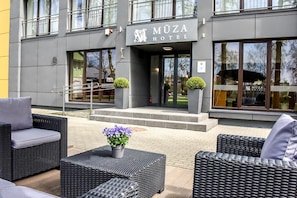 A hotel entrance with a sign reading 'MUZA HOTEL'. There are outdoor wicker furniture and potted plants. - Muza Hotel (Palanga)