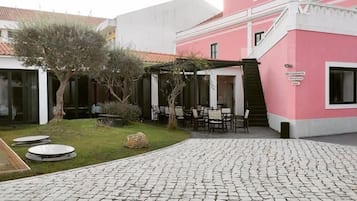 A courtyard with a cobblestone path, outdoor seating, and a building with a pink facade.