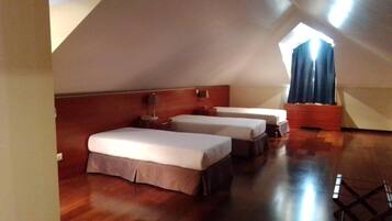 A room with two beds, a wooden floor, a sloped ceiling, and a window with curtains.