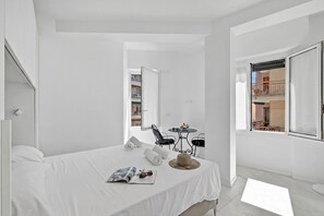 Ein heller Raum mit einem Bett, einer Zeitschrift, Sonnenbrillen, einem Hut und einem kleinen Tisch mit einem Stuhl.