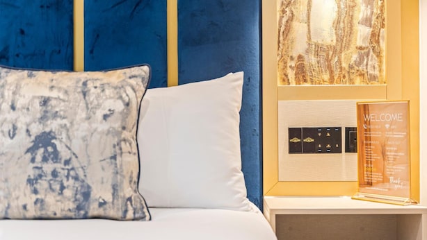 A hotel room with a bed, a white pillow, a welcome sign, and a wall-mounted control panel. - Hotel Holloway (Birmingham)