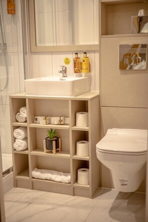 A bathroom with a white sink, shelves with towels and toiletries, a toilet, and a shower area. - Hotel Holloway (Birmingham)