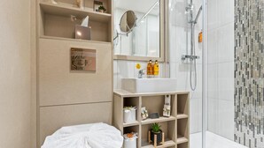 A modern bathroom with a glass shower enclosure, a white sink, and built-in shelves with toiletries and decorative items. - Hotel Holloway (Birmingham)