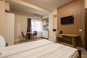 A hotel room with a bed, a desk, a chair, a television, and a kitchenette. - Apart Hotel Bonjour Cluj (Cluj-Napoca)