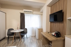 A hotel room with a dining table, two chairs, a TV mounted on the wall, and a small kitchenette area. - Apart Hotel Bonjour Cluj (Cluj-Napoca)