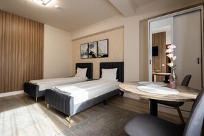 A hotel room with two beds, a dining table, and a wall-mounted TV. - Apart Hotel Bonjour Cluj (Cluj-Napoca)