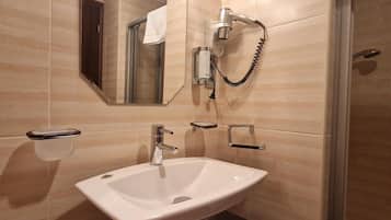 A bathroom with a white sink, a handheld showerhead, a towel rack, and a mirror.