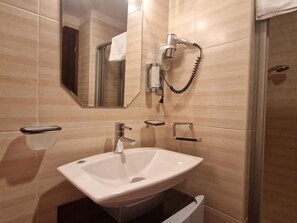 A bathroom with a white sink, a handheld showerhead, a towel rack, and a mirror.