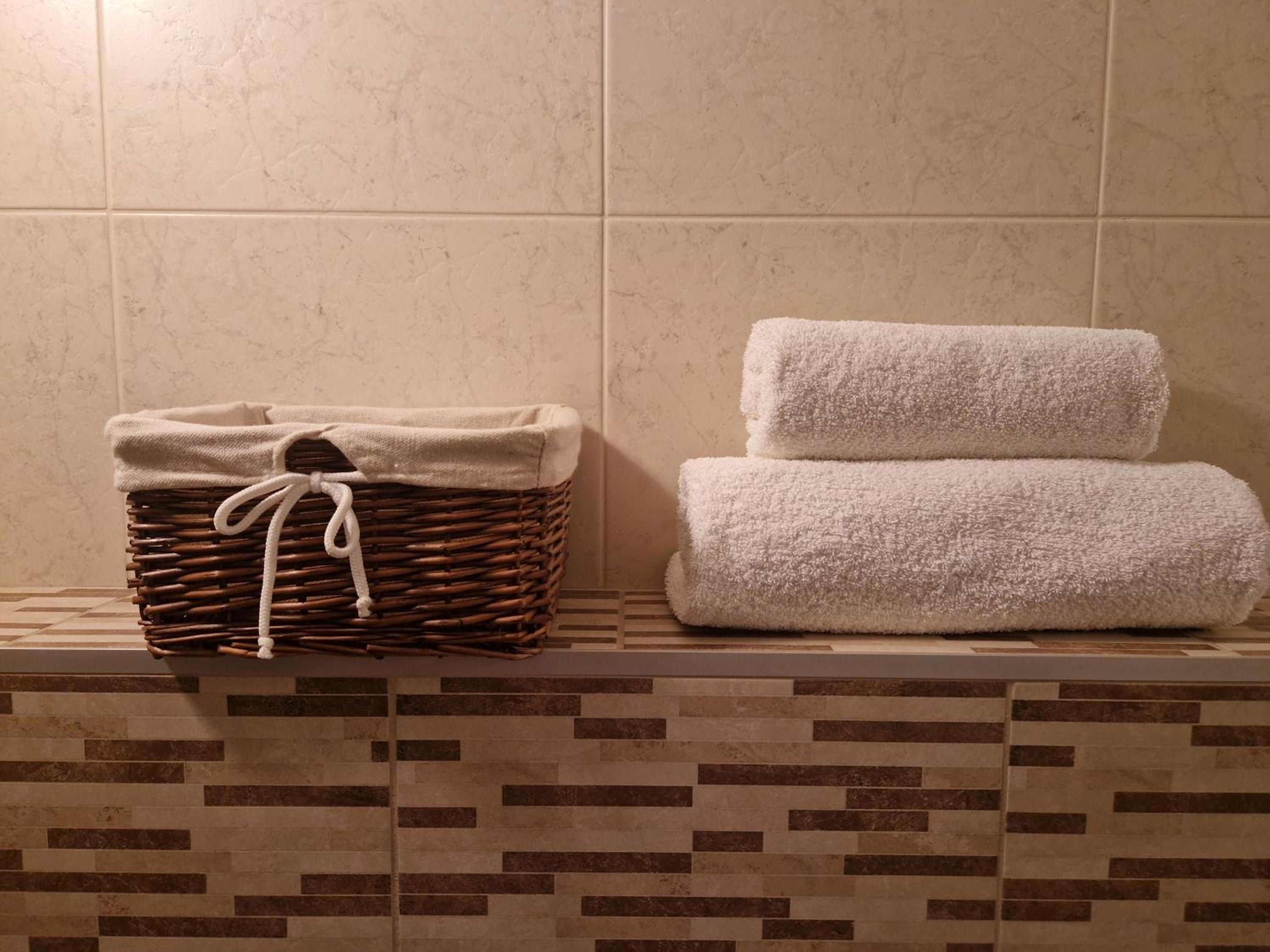 Een badkamer met een betegelde muur, een rieten mand met handdoeken en een betegelde vloer.