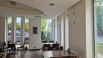 Een eetruimte met tafels en stoelen, grote ramen en uitzicht op de straat.