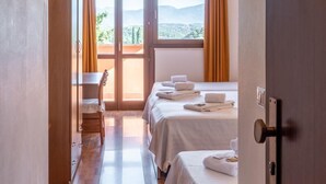 A hotel room with a wooden floor, two beds with white linens, a desk, and a view of the outdoors through large windows. - Hotel La Carica (Pastrengo)