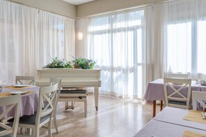 Un coin repas avec un piano, des chaises blanches et des tables dressées pour le repas.