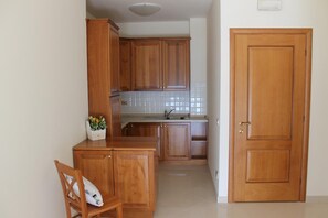 A kitchen with wooden cabinets, a countertop, and a sink. There is a chair and a small table with a flower arrangement. - Lido Resort (Finale Ligure)