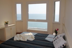 A bedroom with a bed, a dresser, and three windows overlooking the sea. - Lido Resort (Finale Ligure)