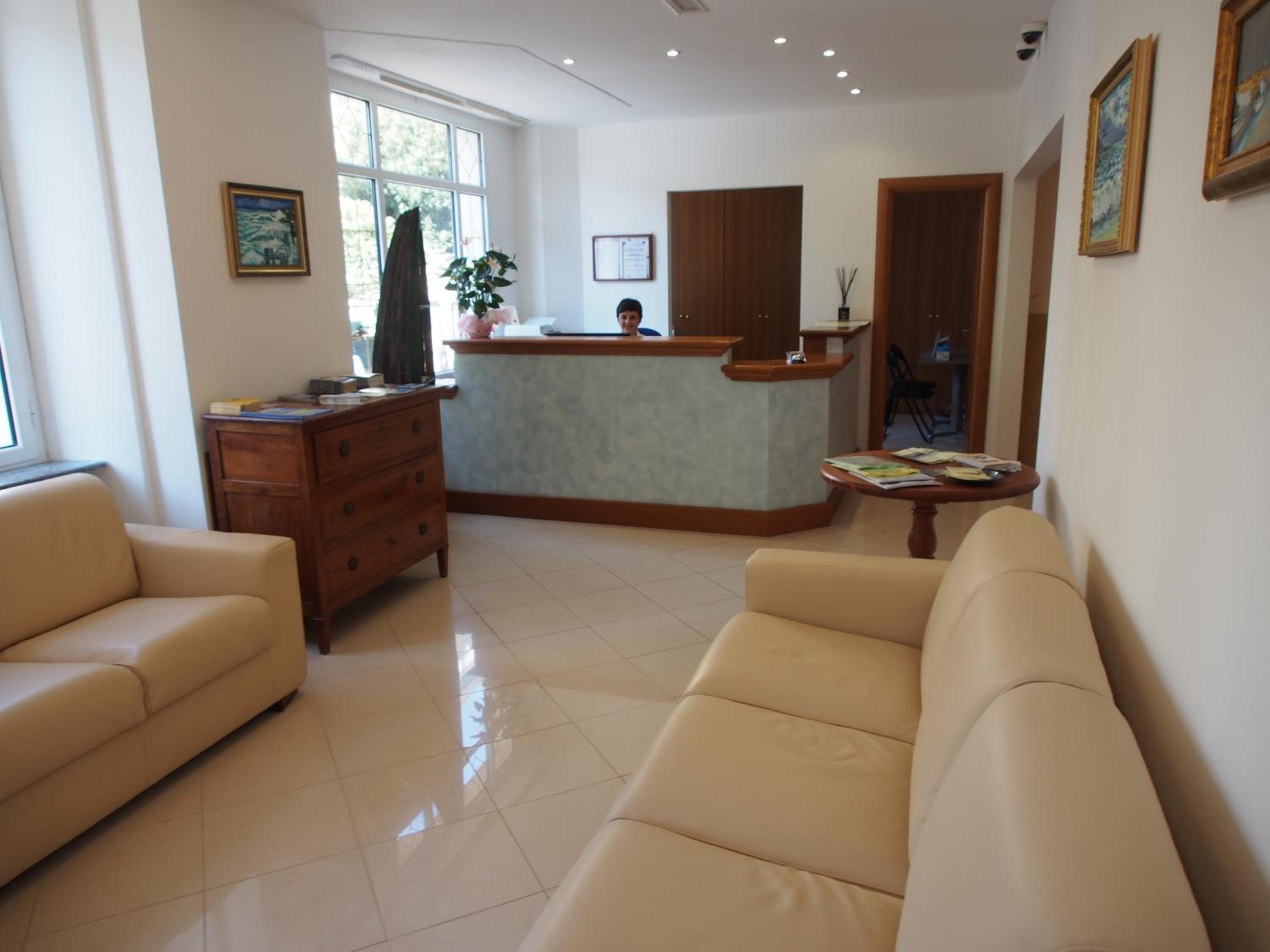 Una hall d'albergo con reception, un divano, un mobiletto in legno e una finestra con vista.