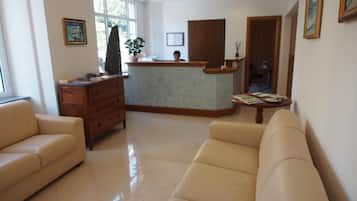 Una hall d'albergo con reception, un divano, un mobiletto in legno e una finestra con vista.