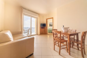 A hotel room with a sofa, a dining table with chairs, a television, and a balcony with a view. - Lido Resort (Finale Ligure)