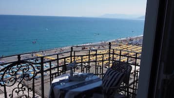 Un balcone con tavolo e sedie che si affaccia su una spiaggia con ombrelloni e persone.