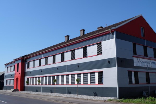 En tvåvåningsbyggnad med en röd och grå fasad, många fönster och en skylt som visar att det är ett hotell.
