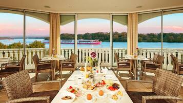 A dining area with a table set for breakfast, overlooking a river with boats.