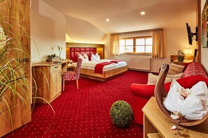A hotel room with a red carpet, a bed with white bedding, a wooden desk, a red sofa, and a small green plant. - Donauhotel Lettnerhof (Naarn im Machlande)