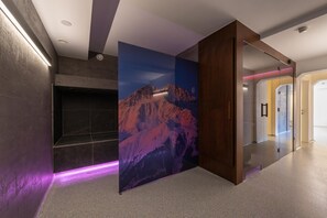 Un interior moderno con un separador de vidrio, un mural de montañas y un pasillo que conduce a una habitación con puerta.
