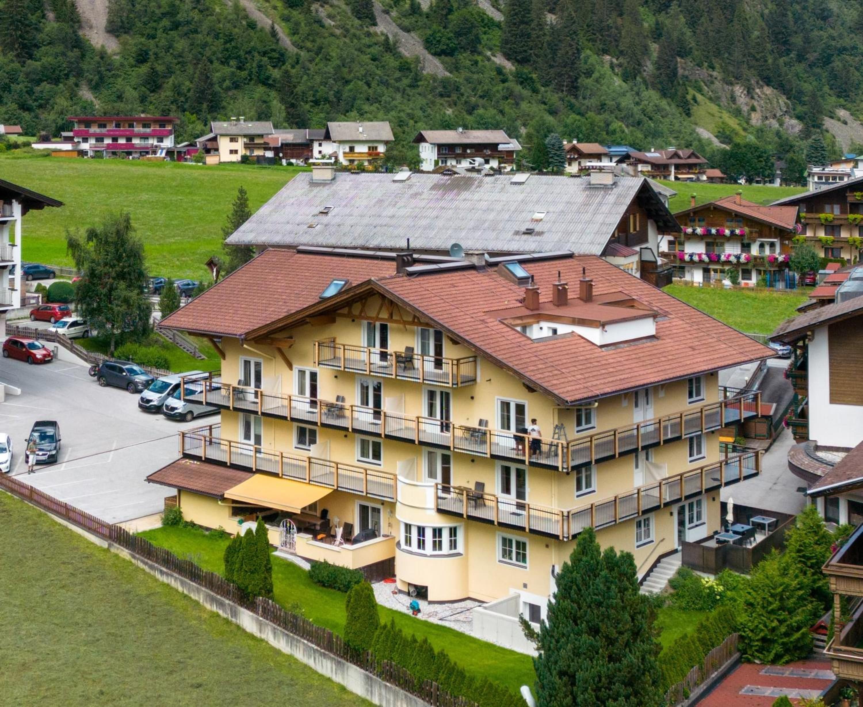 Un hotel de varios pisos con balcones, estacionamiento y montañas al fondo.