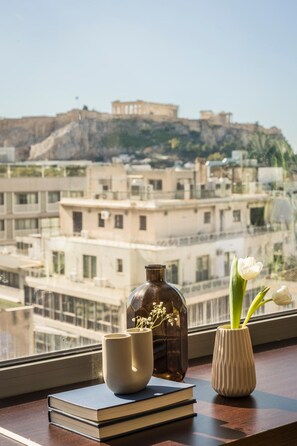 A view of a cityscape with a historical building in the distance, a window with a vase of flowers, and a stack of books on a table. - Aria Acropolis Suites (Athens)