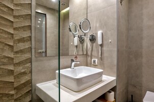 Un baño moderno con lavamanos con recinto de vidrio, un espejo de mano y un teléfono instalado en la pared.