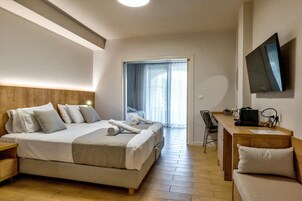 Habitación de hotel con cama, escritorio, silla, televisión y puerta que da a un balcón.