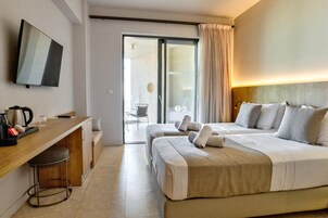 Una habitación de hotel con cama, escritorio, silla, televisión y puerta corredera que da a un balcón.