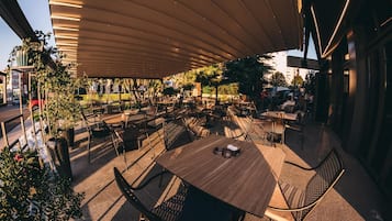 An outdoor dining area with multiple tables and chairs, covered by a large canopy.