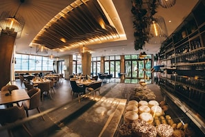 A modern restaurant interior with a bar area, seating arrangements, and a variety of pastries displayed. - Hotel Verso (Mostar)
