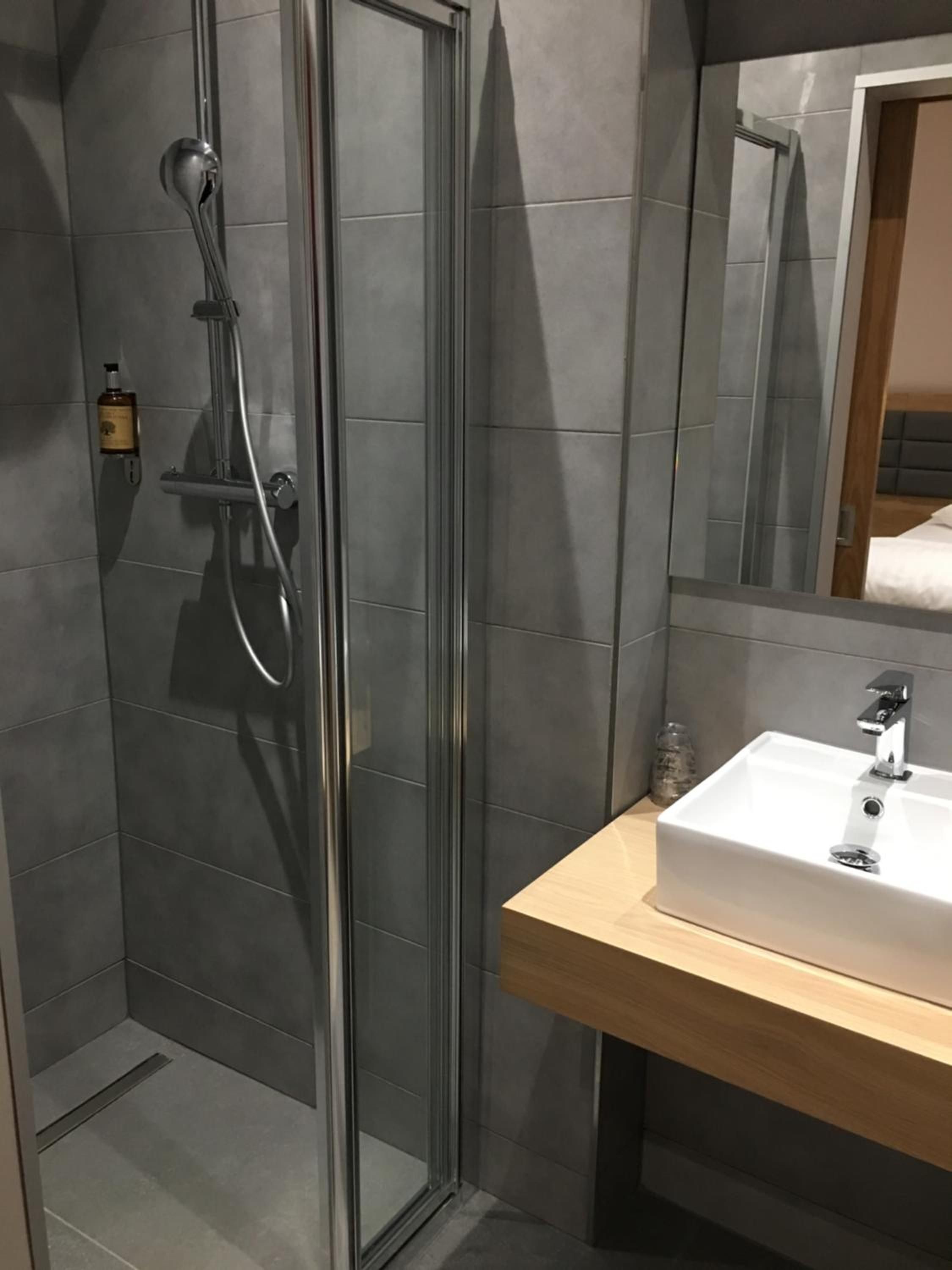 A modern bathroom with a glass shower enclosure, a wooden vanity, and a large mirror.