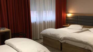 A hotel room with two single beds, a desk, a chair, and a large window with curtains.