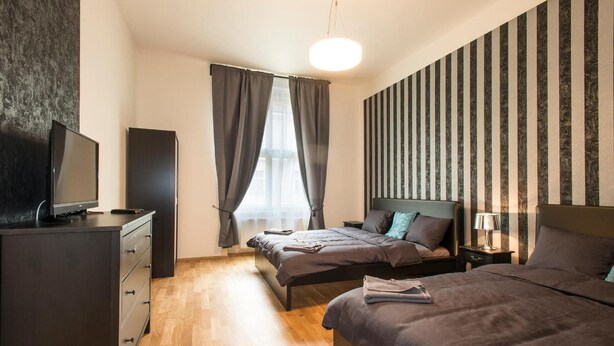 A modern bedroom with a bed, bedside tables, a dresser, and a television. - Neklanova Apartments (Prague)