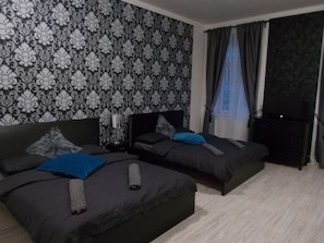 A hotel room with two beds, a patterned wallpaper, a nightstand with a lamp, and a TV. - Neklanova Apartments (Prague)