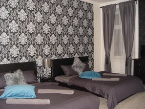 A hotel room with two beds, a patterned wallpaper, a nightstand, and a window with curtains. - Neklanova Apartments (Prague)