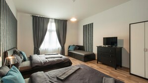 A modern bedroom with two beds, a TV, a dresser, and a window with curtains. - Neklanova Apartments (Prague)