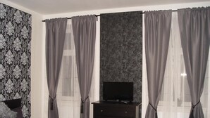 A bedroom with a bed, a dresser, a television, and curtains. - Neklanova Apartments (Prague)