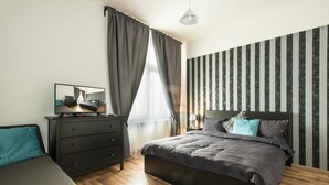 A modern bedroom with a bed, a dresser, a TV, and a striped wall. - Neklanova Apartments (Prague)