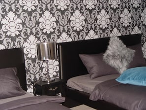 A bedroom with a patterned wallpaper, a bedside lamp, a dark headboard, and multiple pillows. - Neklanova Apartments (Prague)