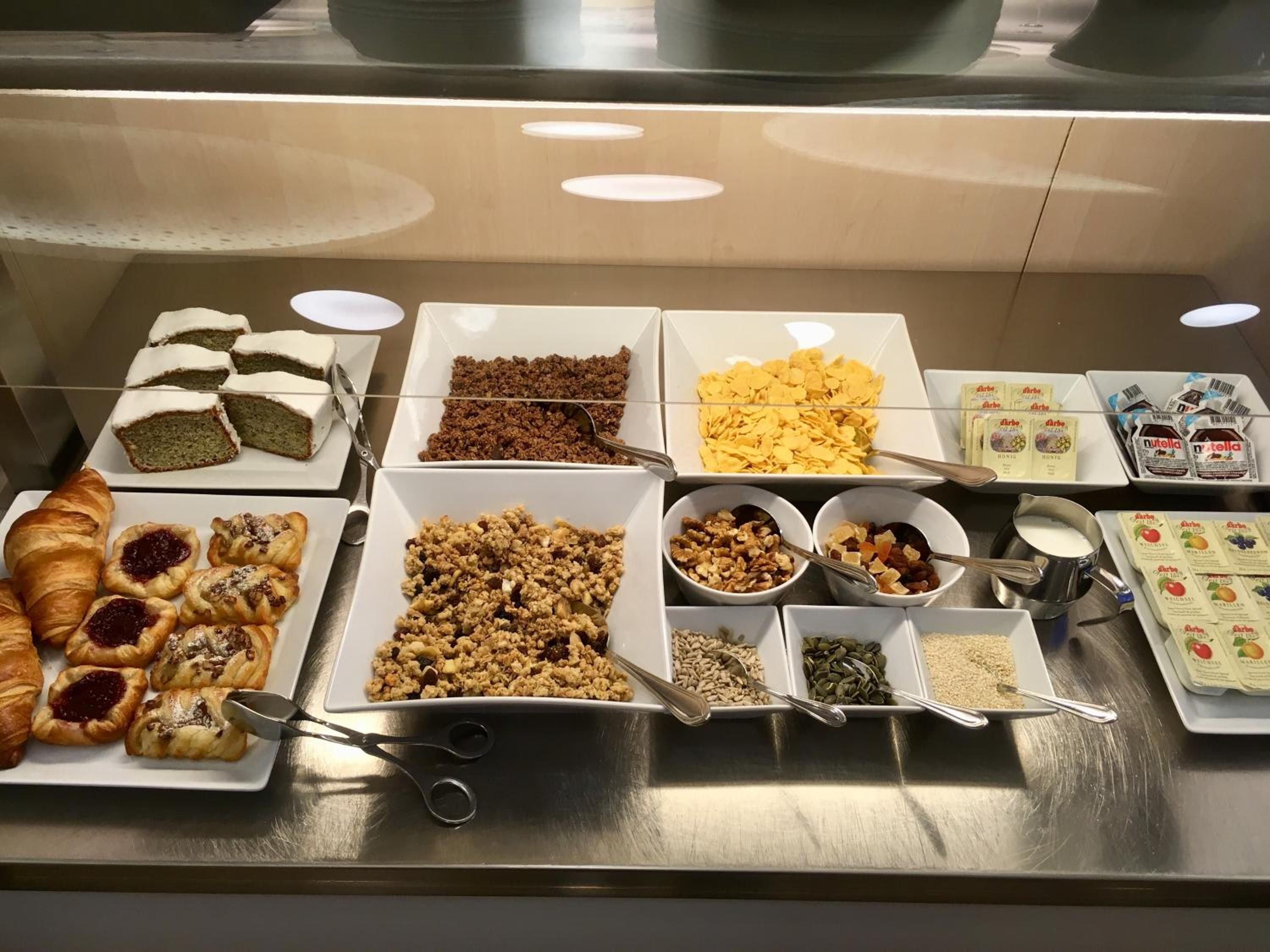 A buffet with various food items including pastries, cereals, and spreads.
