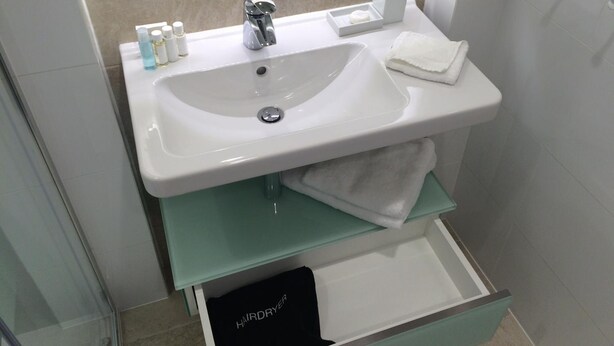 A bathroom with a white sink, a mirror, a towel, and a drawer with a black item labeled 'HAIRDRYER'. - Hotel Erwin Junker (Holice)