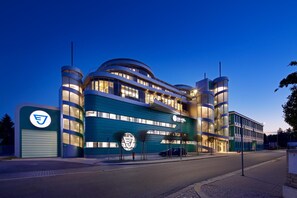 A modern building with a curved facade, multiple balconies, and a prominent logo on the entrance. - Hotel Erwin Junker (Holice)