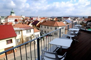 Un balcón con vistas a un pueblo, con edificios de techos rojos y una estructura en forma de cúpula verde.